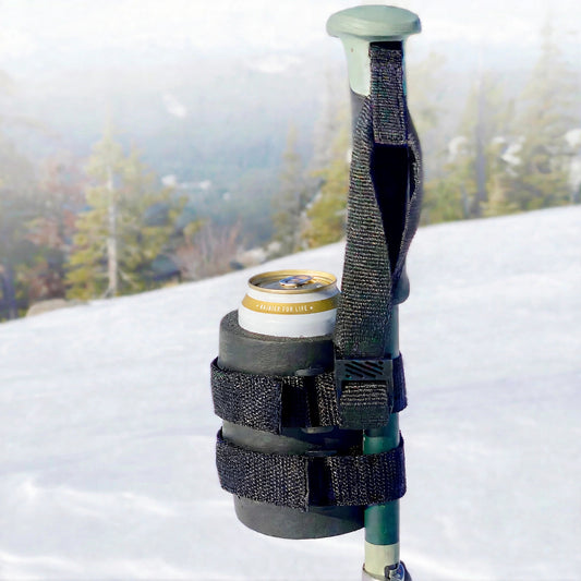 Black beer can holder strapped to a ski pole, holding a Rainier beer can with snowy mountains behind it.