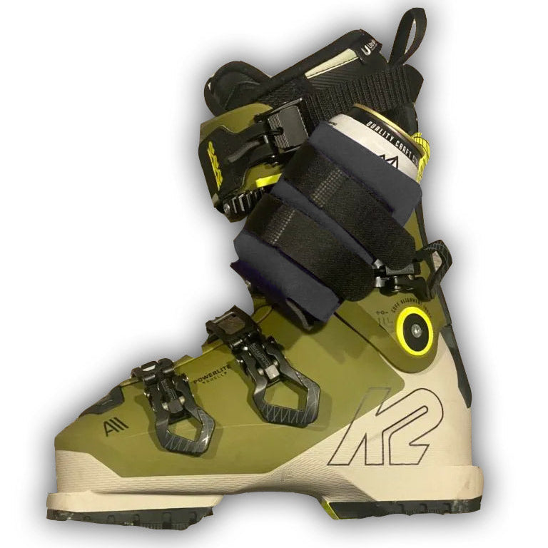 Black beer can holder strapped around a ski boot's buckles on a white background.