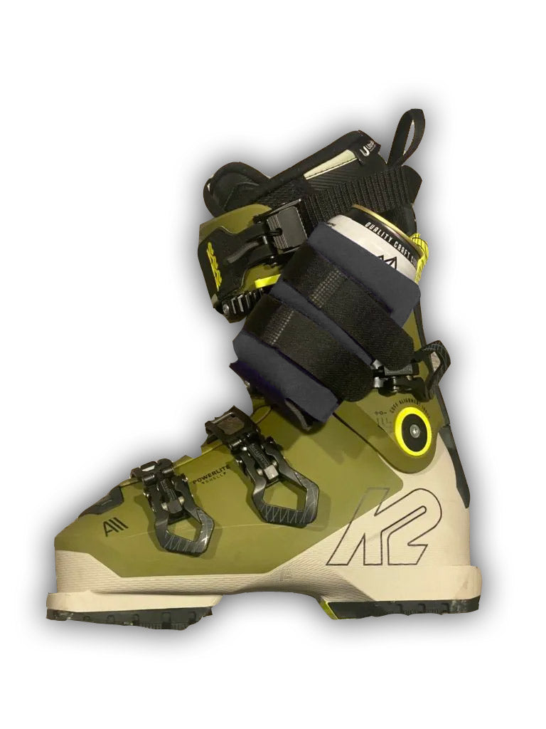 Black beer can holder strapped around a ski boot's buckles on a white background.