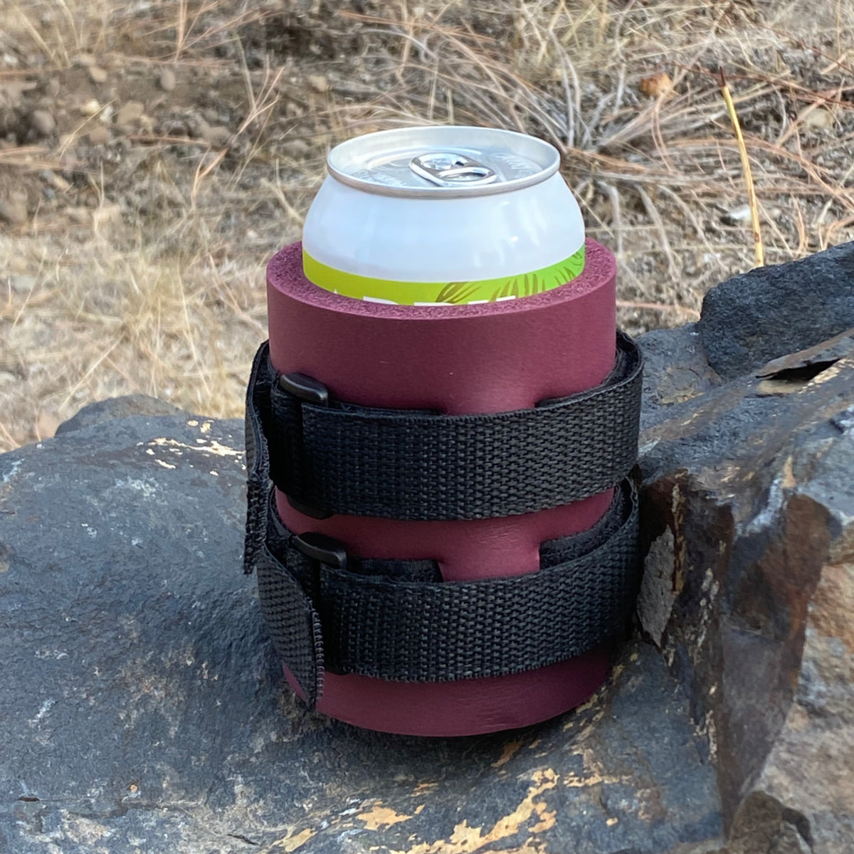Burgundy Beer Binding PRO can holder with black straps, holding a can on a rock outdoors.