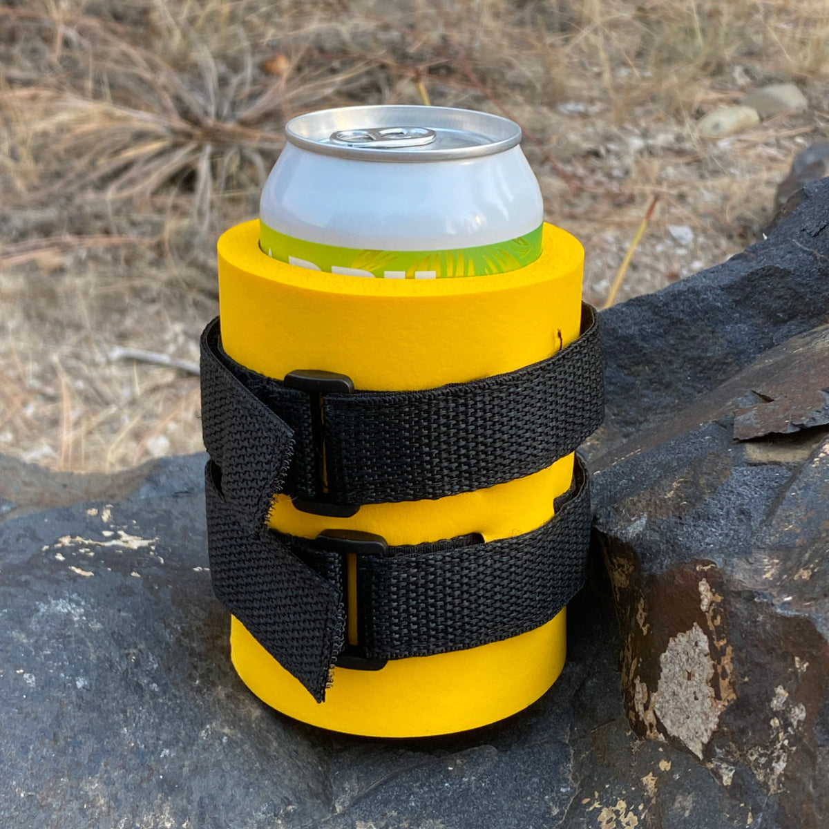 Yellow Beer Binding PRO can holder with black straps, holding a can on a rock outdoors.