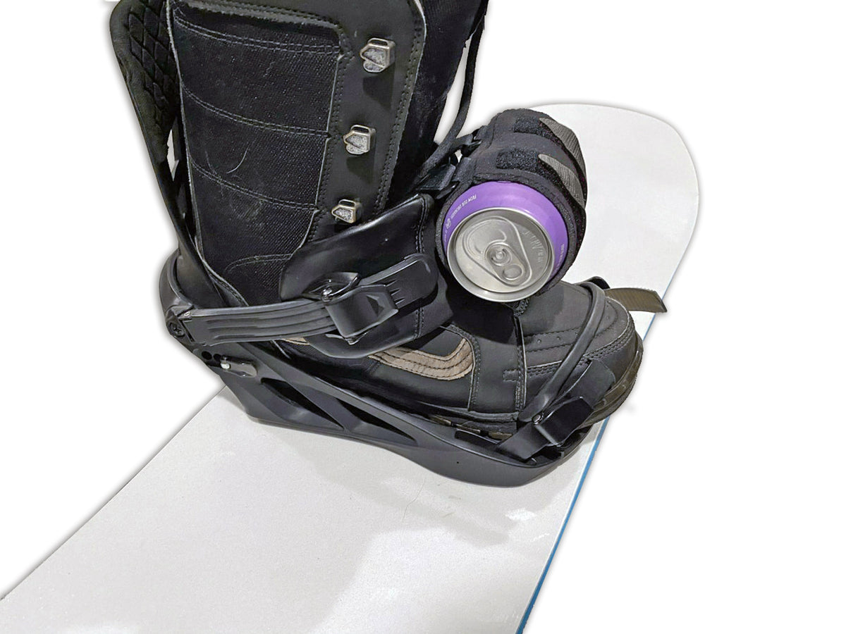 Studio close-up of the black beer can holder strapped to a snowboard binding's front strap, holding a can.