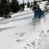 Skier ripping powder turn with beer attached to ski pole