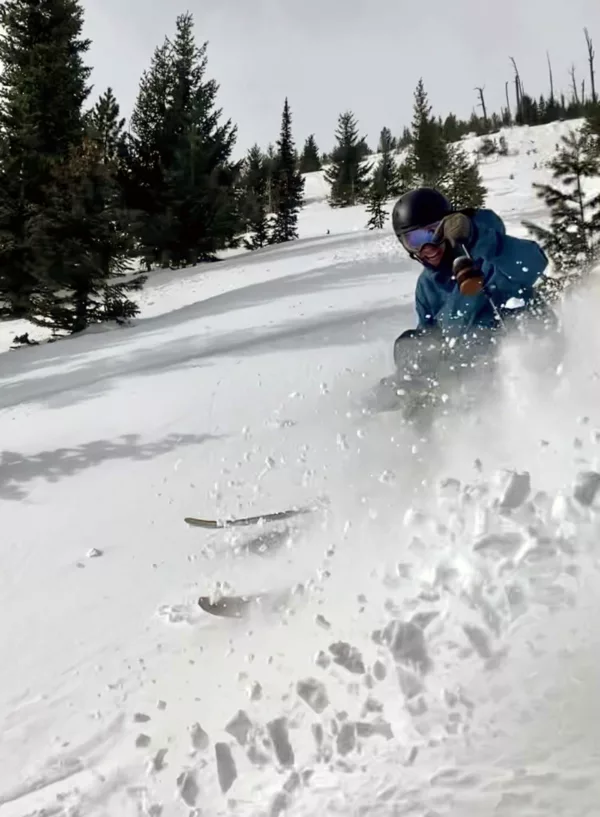 Skier ripping powder turn with beer attached to ski pole